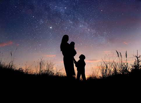 Silhouette of mother and her two little children against starry night sky